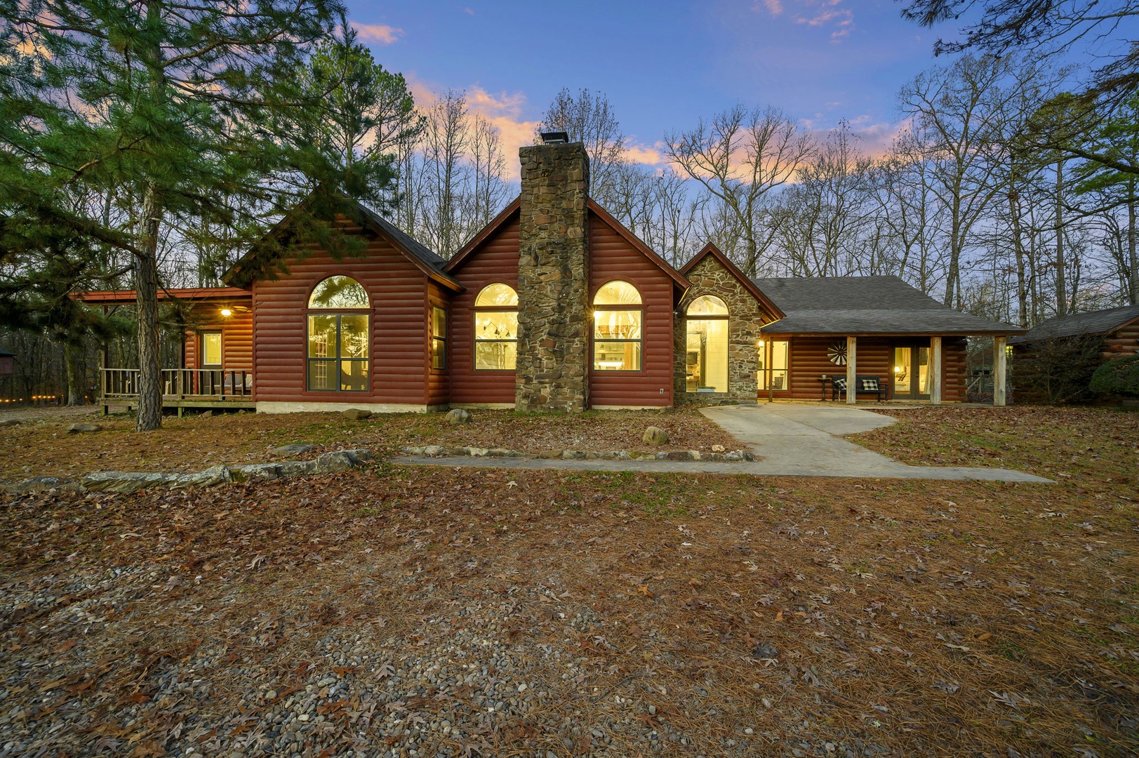 Beautiful log cabin nestled among towering trees, featuring warm stone chimney and welcoming lit windows at twilight.