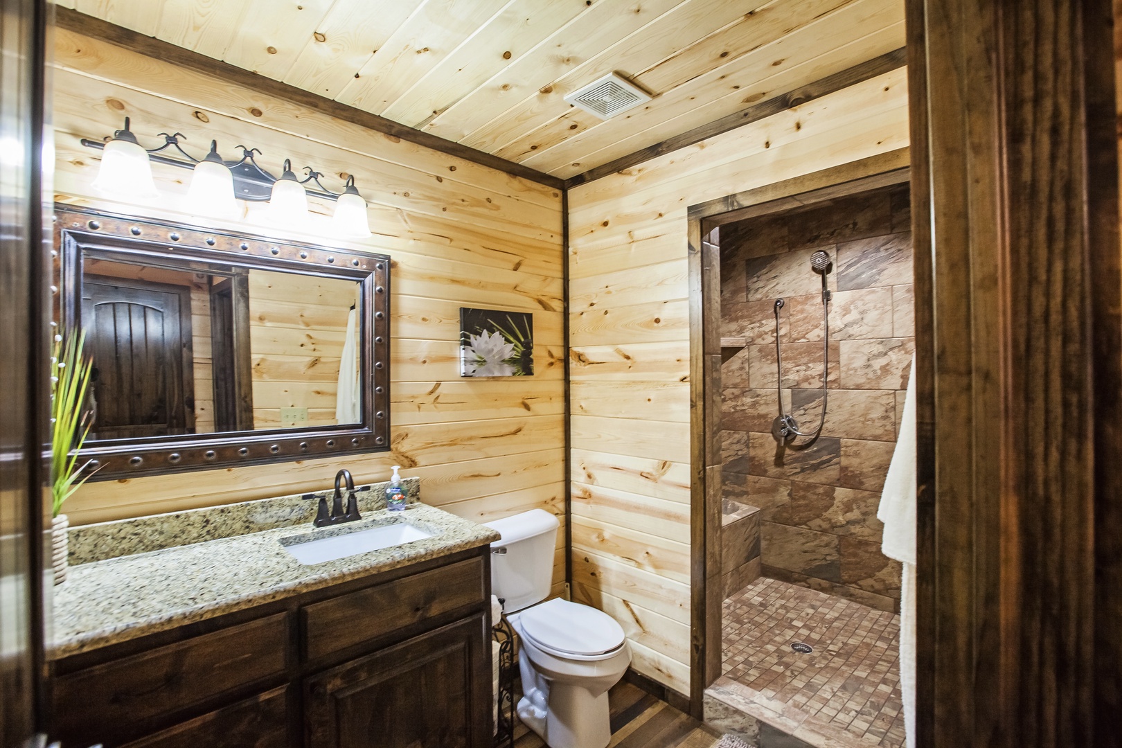 Step into your rustic retreat's spa-like bathroom, where knotty pine walls and stone shower create a perfect mountain getaway ambiance.