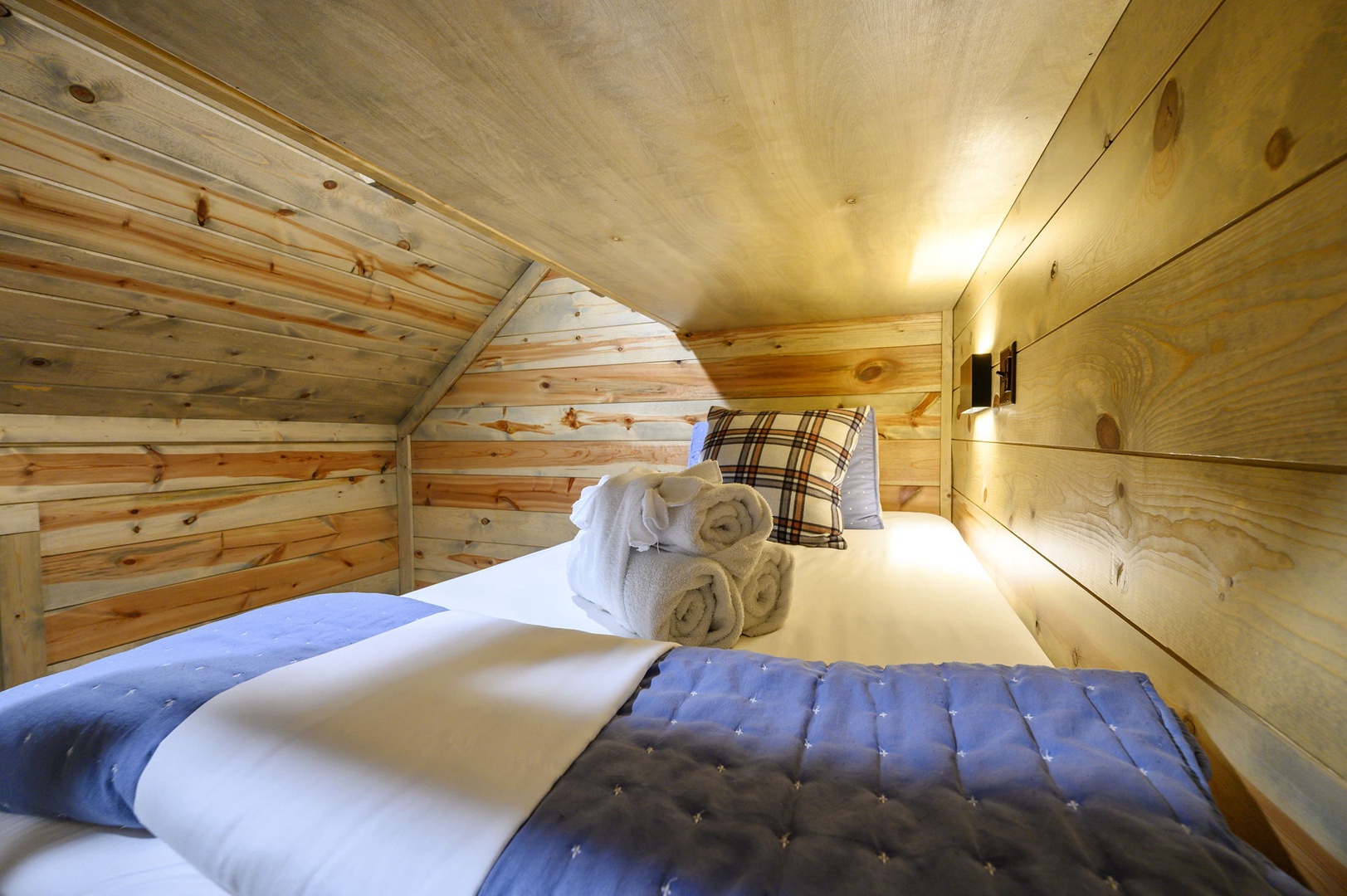 Slip into your cozy loft bedroom, wrapped in warm pine and soft linens. The rustic wood walls and sloped ceiling create an intimate retreat where you can truly unwind.