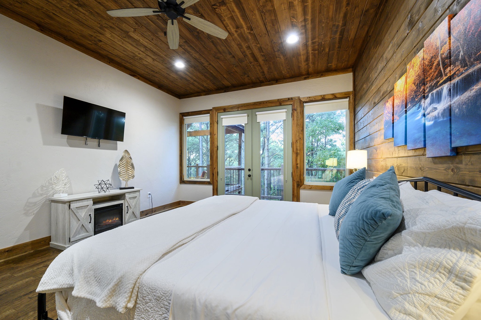Sink into plush bedding beneath a stunning wood-paneled ceiling, with your own fireplace glowing softly and glass doors opening to a private balcony surrounded by trees.