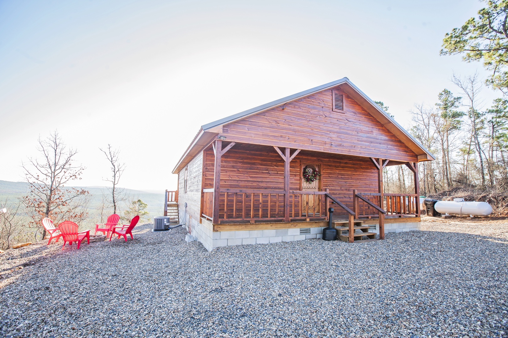 Charming log cabin with covered porch and red chairs overlooking mountain views in a peaceful wooded setting.