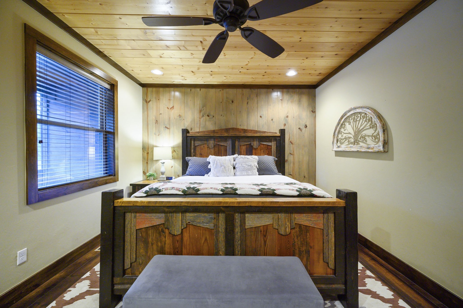 Retreat to this cozy bedroom where rustic wood paneling and a handcrafted bed invite you to unwind. Natural light streams through the window, while a ceiling fan keeps your space perfectly comfortable.
