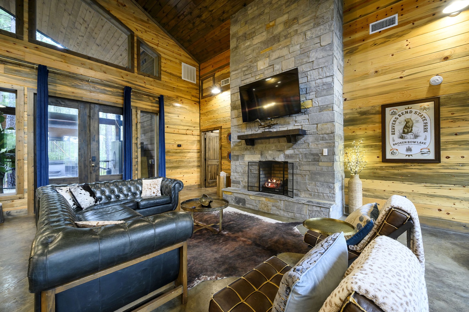 Unwind in your spacious living room, where soaring wood-beamed ceilings and a stunning stone fireplace create a warm, cabin-lodge ambiance. Sink into plush leather seating for cozy evenings by the fire.
