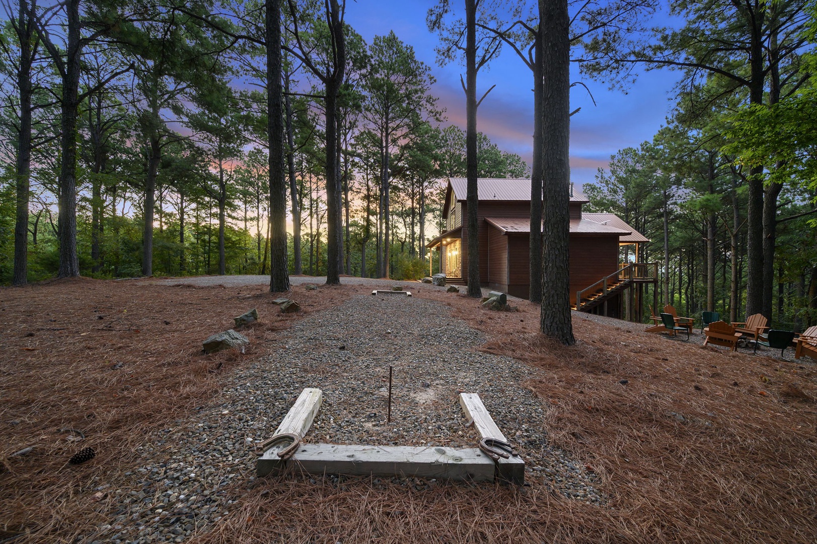 This vacation rental is nestled among tall pines in a peaceful wooded setting, with a horseshoe pit and outdoor seating for enjoying warm evenings under the trees.