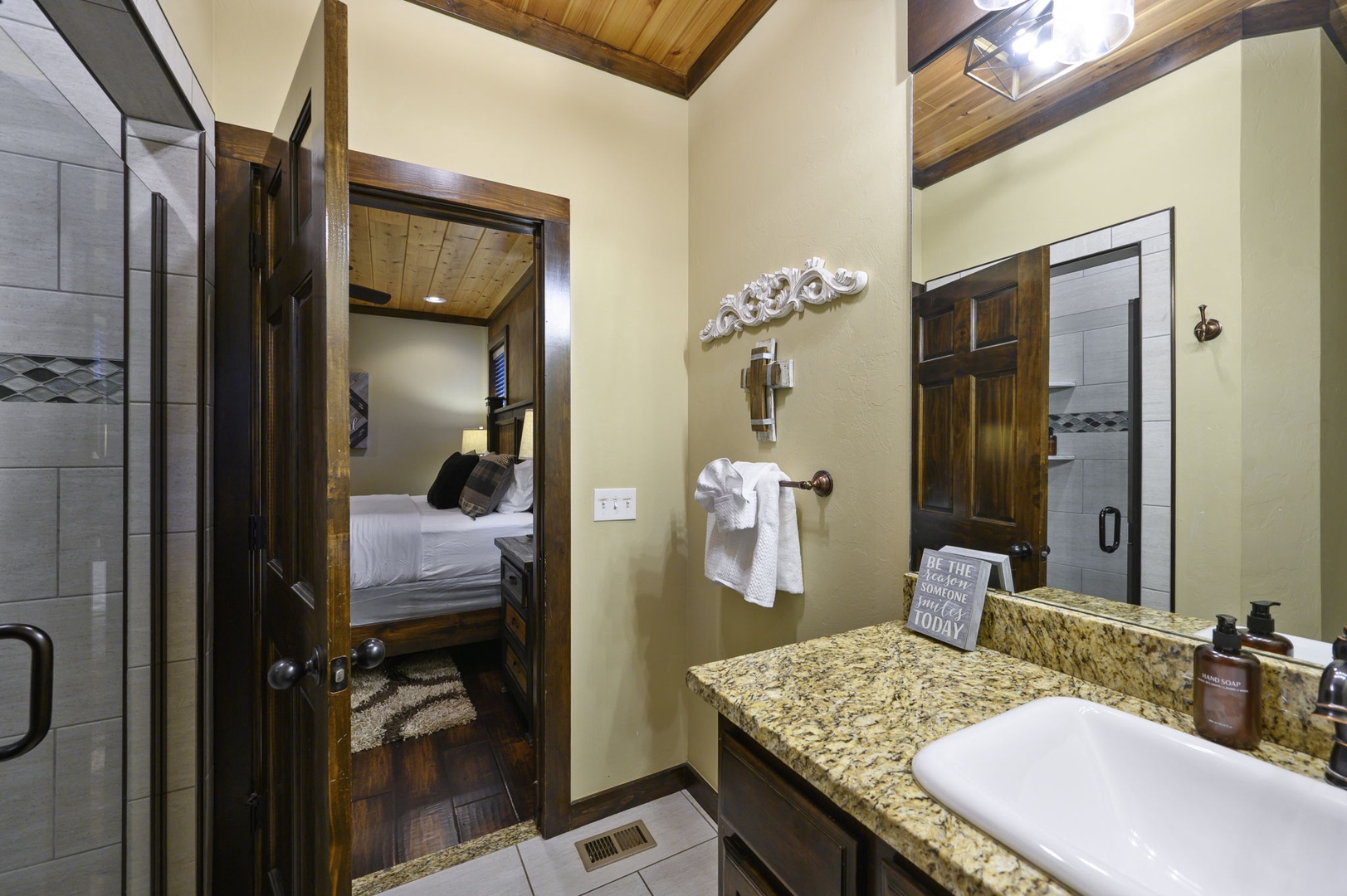 Your private bathroom features granite countertops, fresh towels, and rustic wood accents, with soft lighting and a welcoming doorway to your cozy bedroom retreat.