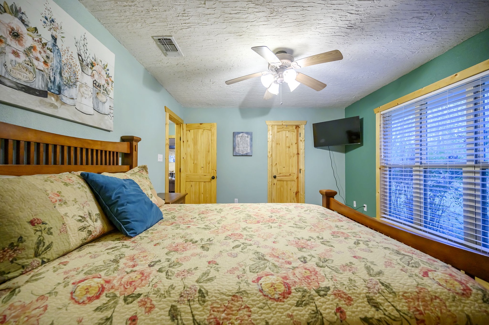 Drift off in your cozy bedroom with soft floral bedding, rustic wood doors, and gentle ceiling fan keeping you comfortable all night.