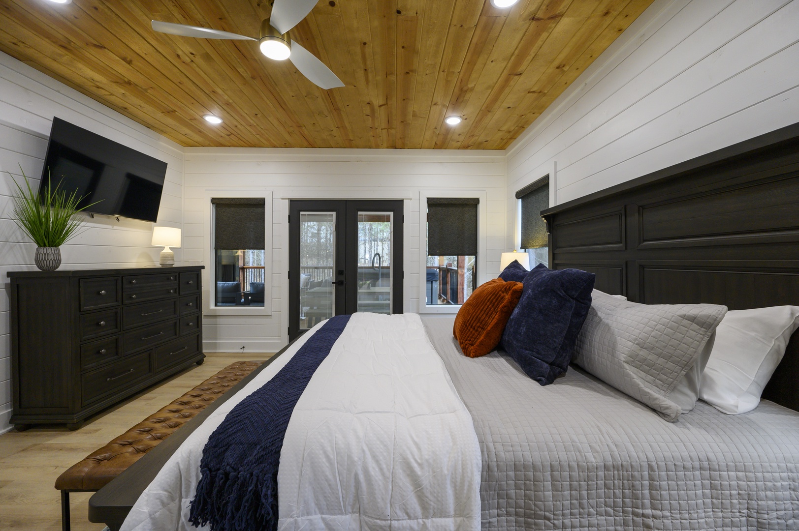 Unwind in this beautifully crafted bedroom featuring warm wood ceilings, cozy linens, and French doors opening to your private deck.