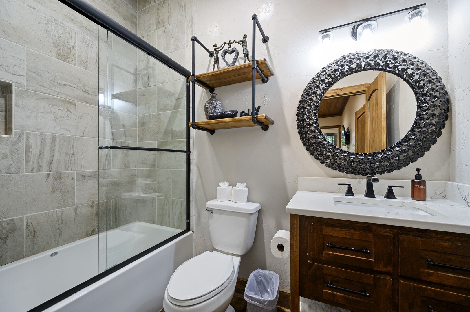 Step into a spa-like bathroom with warm, neutral tones and industrial-chic details. A walk-in shower invites you to unwind, while the statement mirror and thoughtfully arranged shelving add personality and charm to your private retreat.