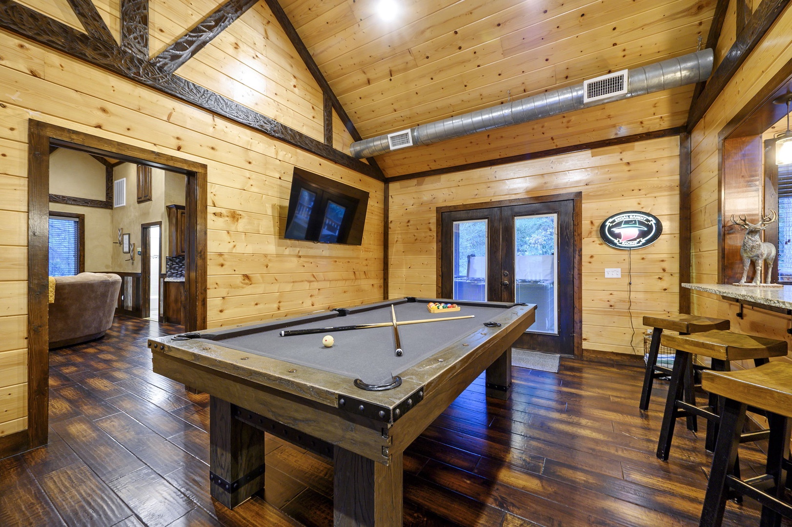 Gather your group for friendly competition in this rustic game room, featuring a full-size billiard table under soaring vaulted ceilings with exposed timber beams and warm wood paneling throughout.