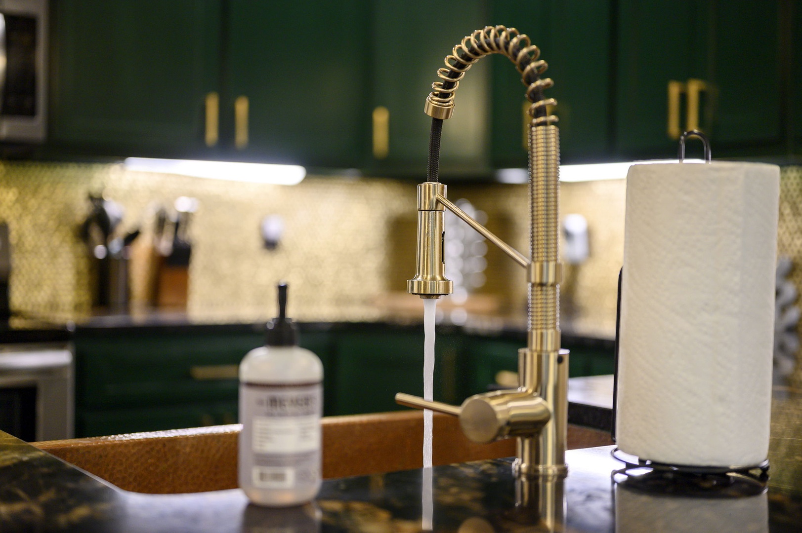 Your kitchen features elegant gold hardware and modern fixtures against rich green cabinetry—perfect for preparing meals in style.