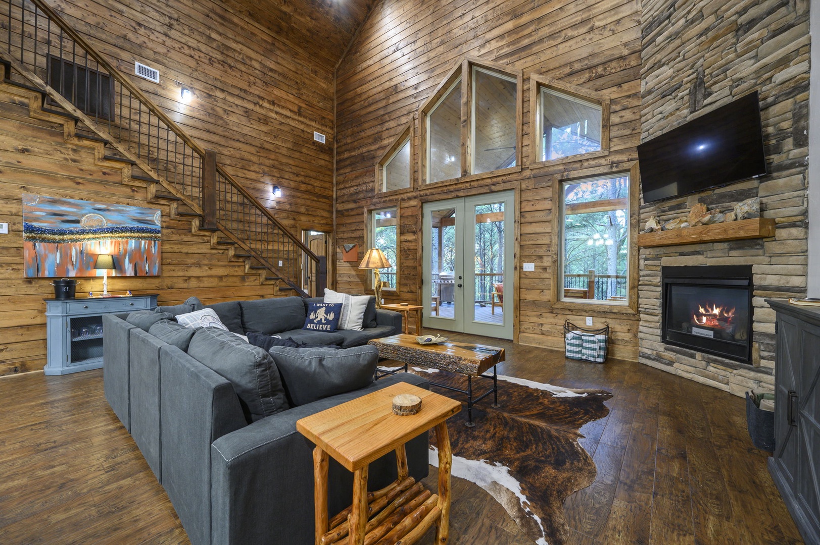 Unwind in your spacious living room, where soaring wood-paneled ceilings, a crackling stone fireplace, and floor-to-ceiling windows create a warm mountain retreat perfect for relaxing after exploring the outdoors.