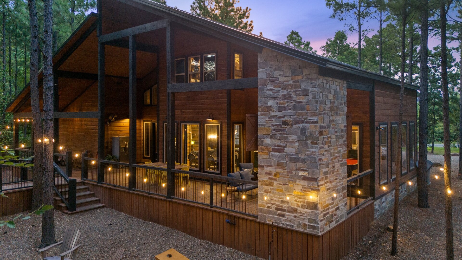 Modern cabin nestled among towering pines, its warm lights beckoning as dusk settles into evening. Stone and wood architecture blends seamlessly with the natural landscape.