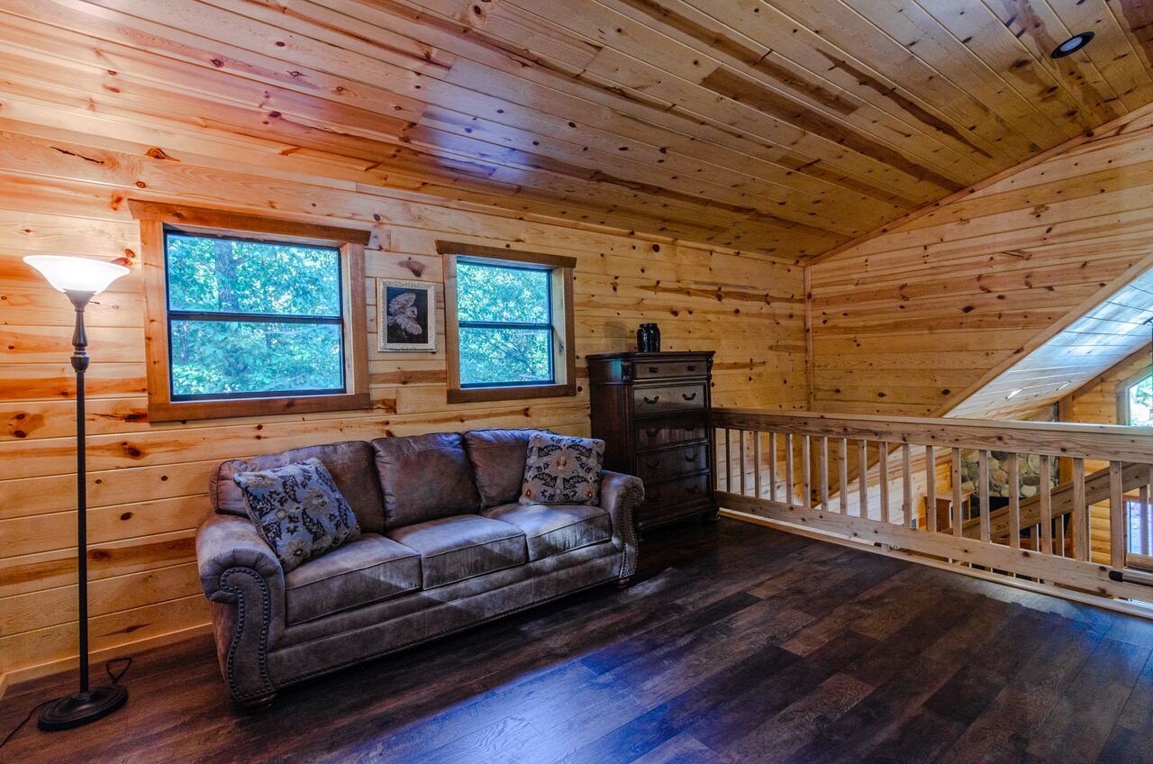 Relax in your cozy loft retreat, where warm wood surrounds you and forest views peek through the windows. Sink into the plush sofa and unwind completely.