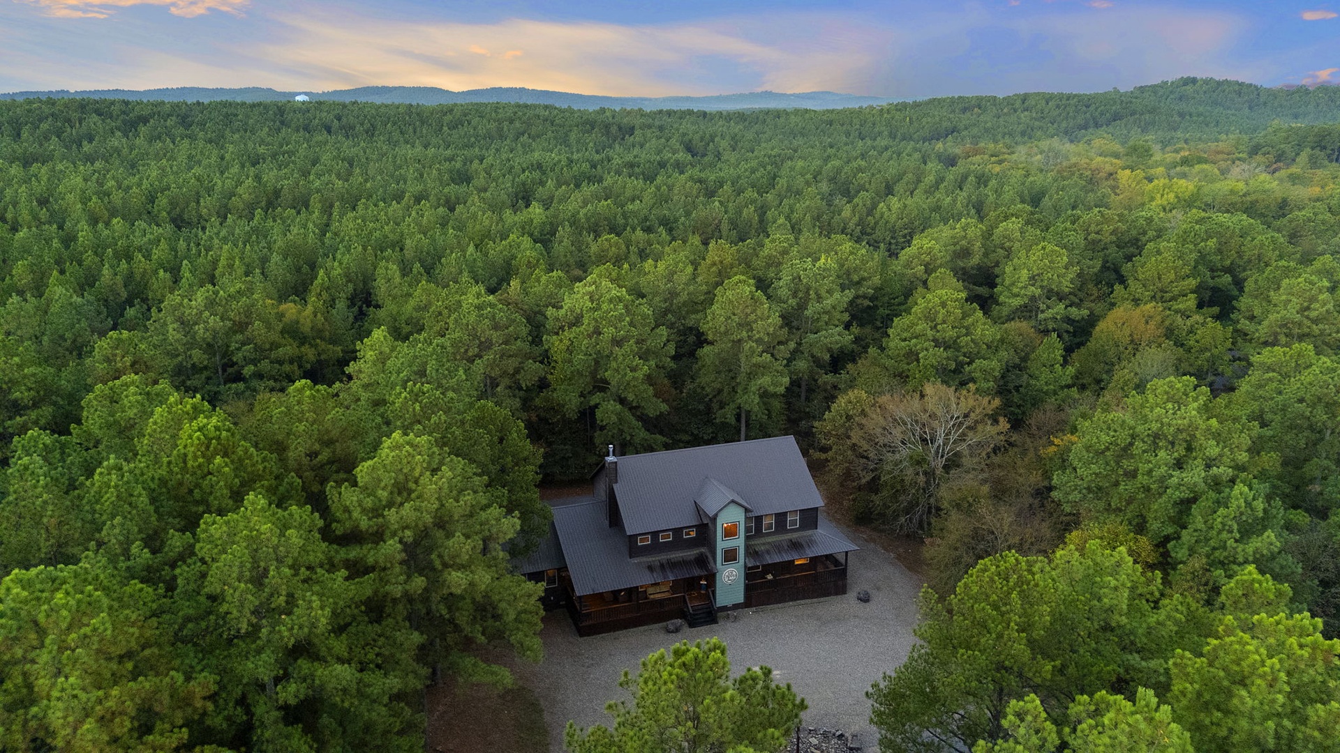 Aerial view of the property nestled among rolling forested hills, offering a peaceful, secluded mountain setting with ample parking and natural beauty.