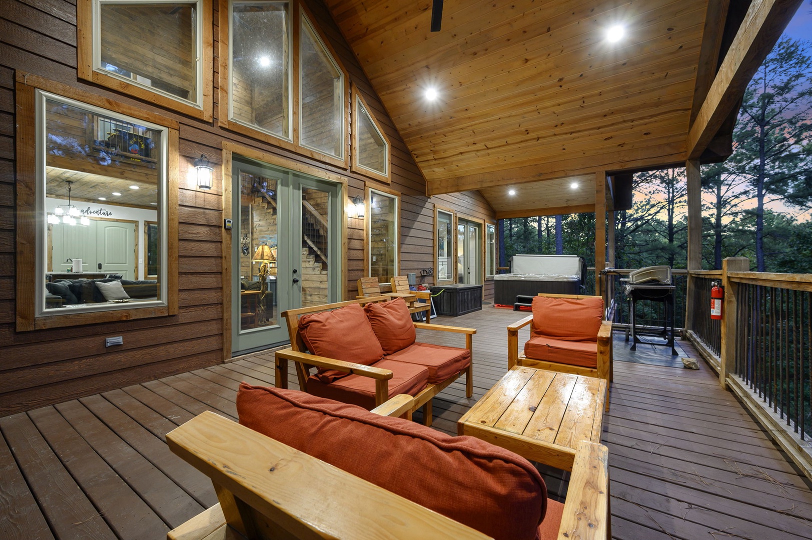 Your private covered deck invites you to unwind on plush seating while soaking in the hot tub, surrounded by peaceful forest views at dusk.
