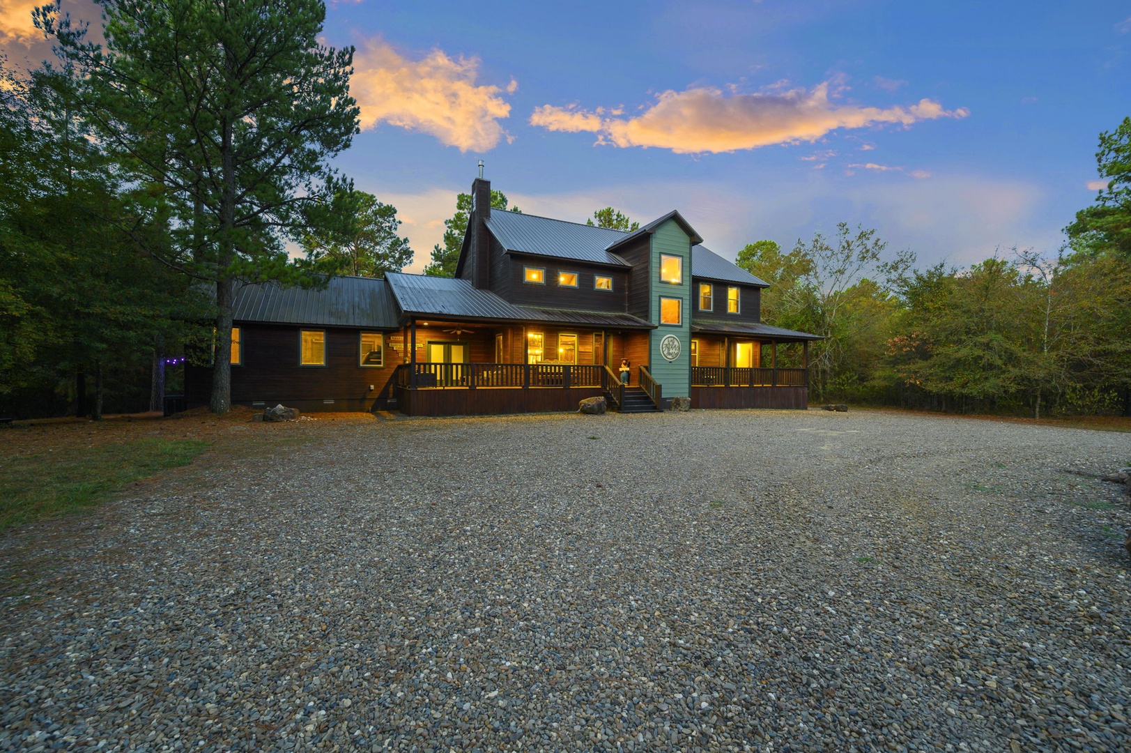 A spacious, contemporary lodge framed by natural woods and vibrant evening light, with ample parking and an inviting entrance at the heart of a serene, wooded area.