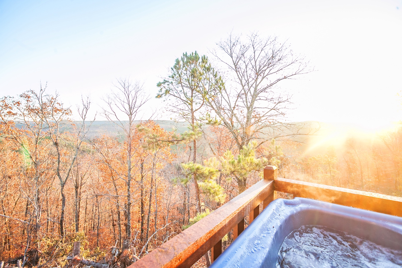 Stunning autumn forest views surround the elevated hot tub deck with golden sunlight filtering through colorful fall foliage.