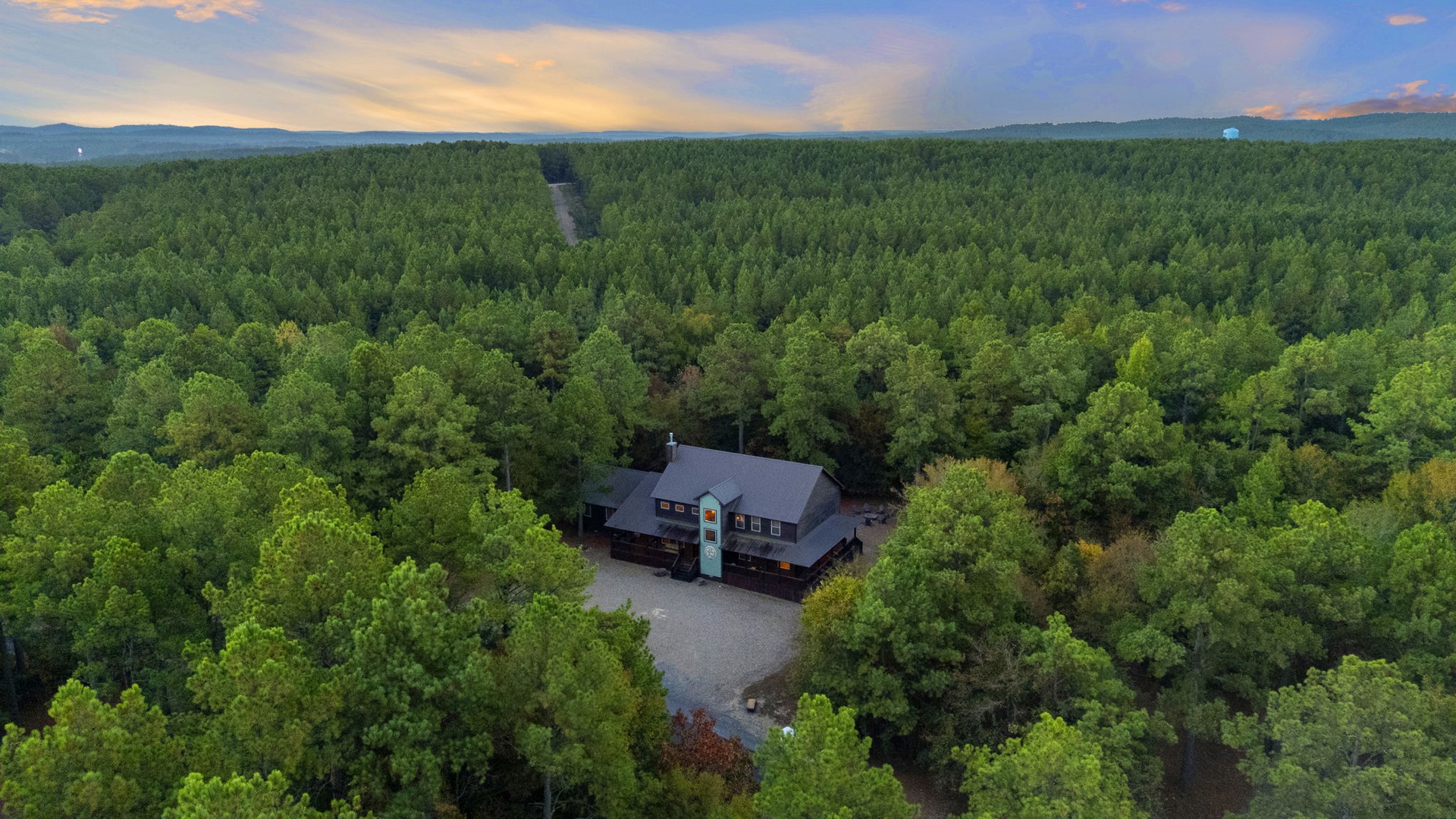 Aerial view of a secluded mountain retreat nestled in lush forest with private access road and surrounding natural landscape.