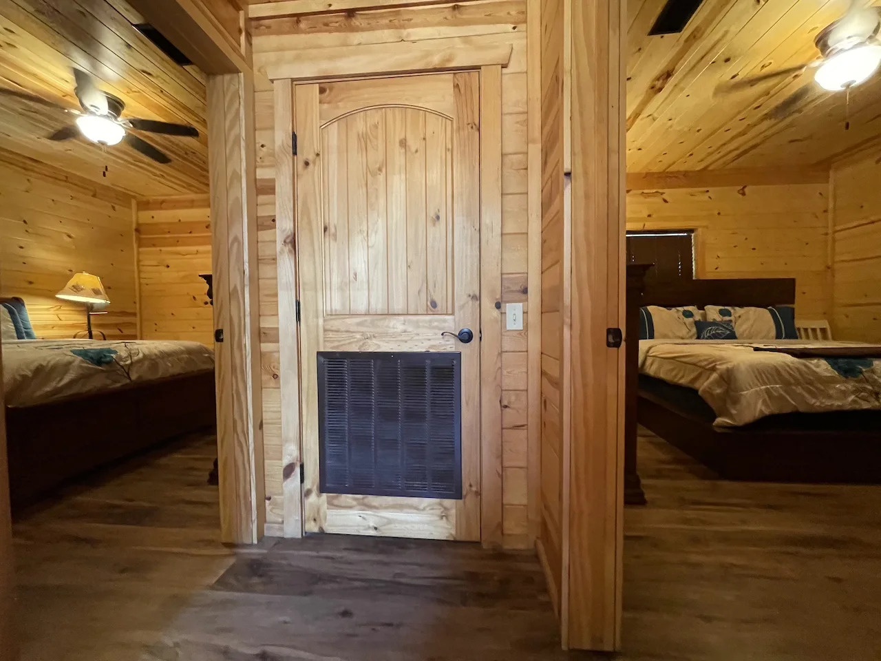 Step into your cozy mountain retreat with warm pine walls and two inviting bedrooms separated by rustic doors, all glowing under soft lighting that makes the cabin feel like home.