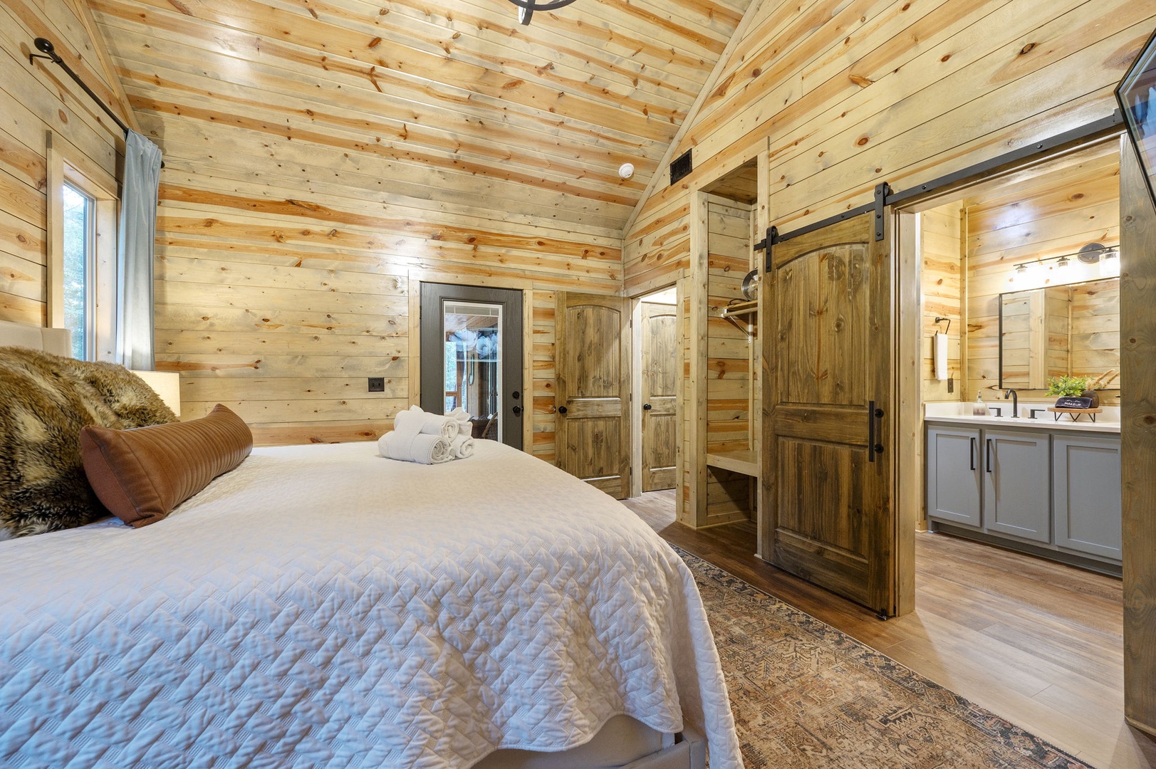 Unwind in your cozy bedroom, where vaulted wood-planked ceilings and rustic barn doors create a warm, cabin-inspired retreat. Slide into crisp linens and let the charm of natural textures surround you.