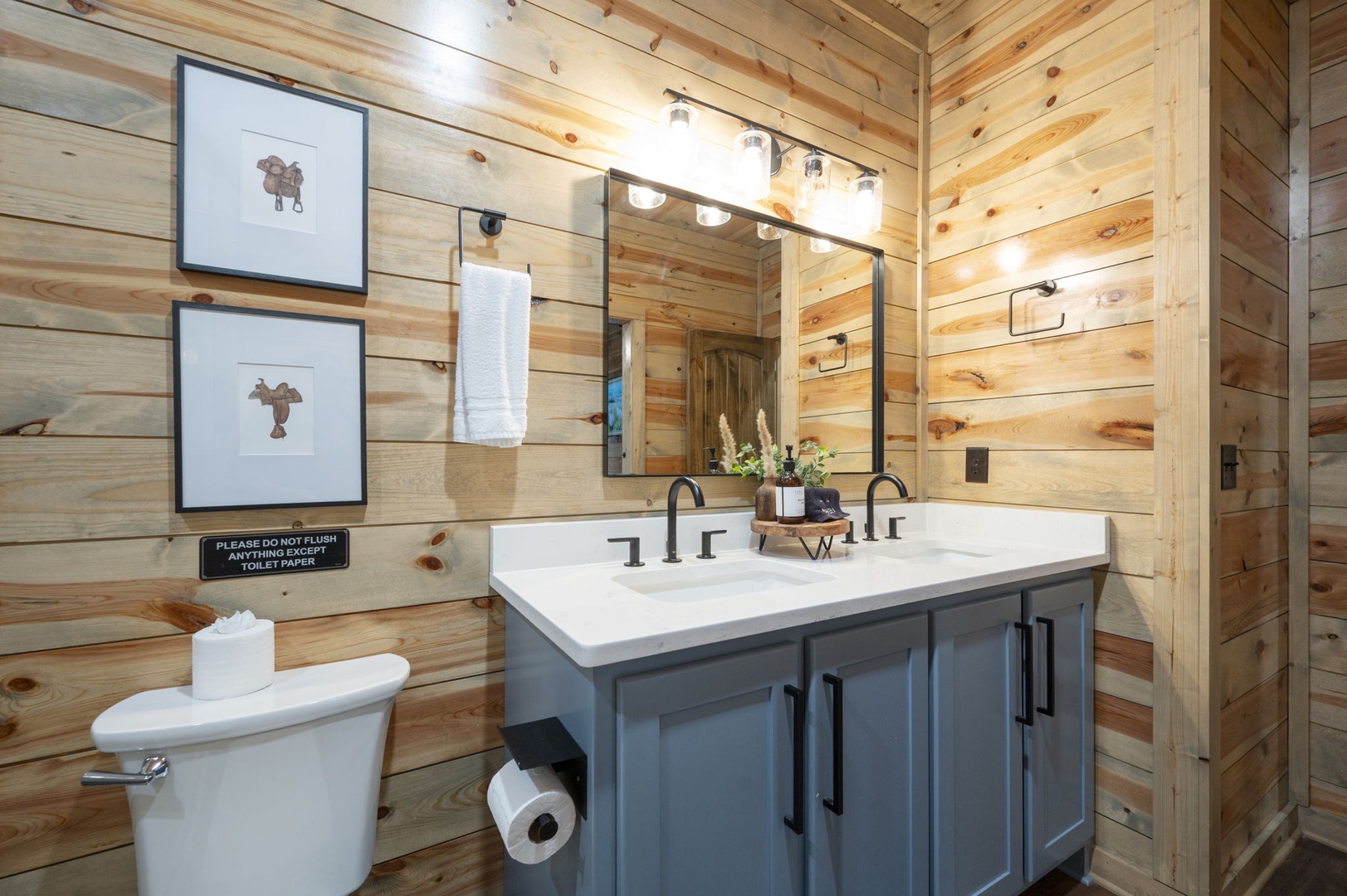 Step into your own private retreat with rustic wood walls, a stylish vanity with dual sinks, and thoughtful touches like fresh flowers and western-inspired art that make freshening up feel special.