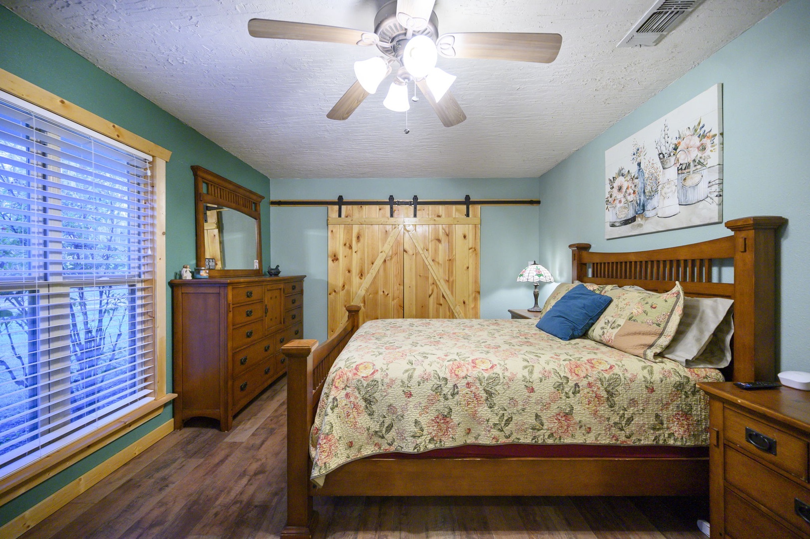 Rest peacefully in your cozy bedroom featuring warm wood furnishings, a rustic barn door, and soothing blue walls that create the perfect retreat.