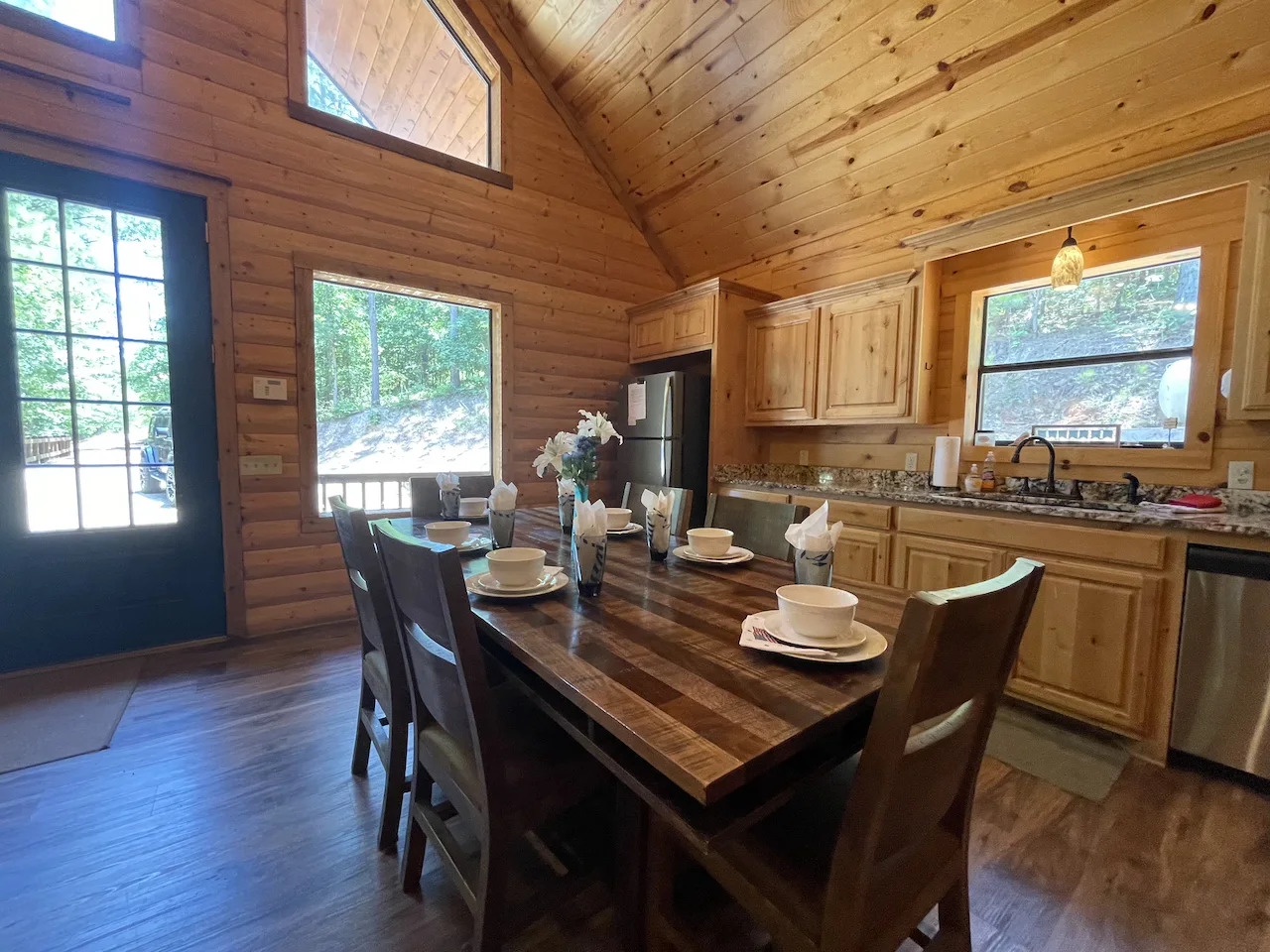 Gather around this handcrafted dining table in your cozy mountain cabin, where warm wood surrounds you and natural light pours through oversized windows. Your fully equipped kitchen awaits, ready for home-cooked meals in this serene woodland retreat.