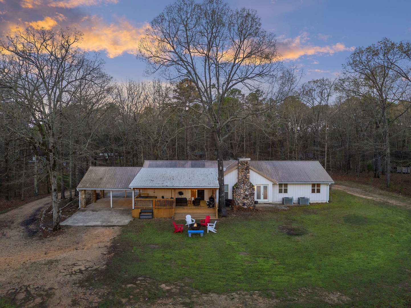 Rural retreat with a wraparound porch, and colorful seating area nestled among towering trees.
