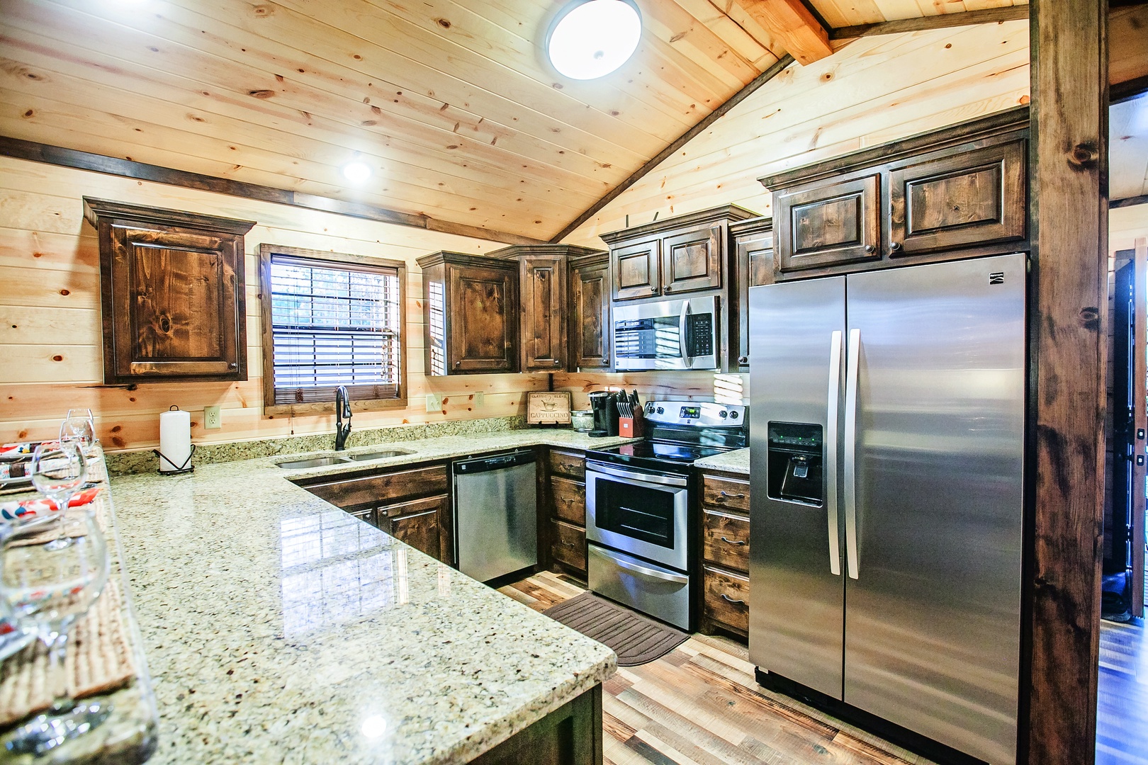 Your rustic dream kitchen awaits with granite countertops, stainless steel appliances, and warm wood cabinetry under soaring timber ceilings.