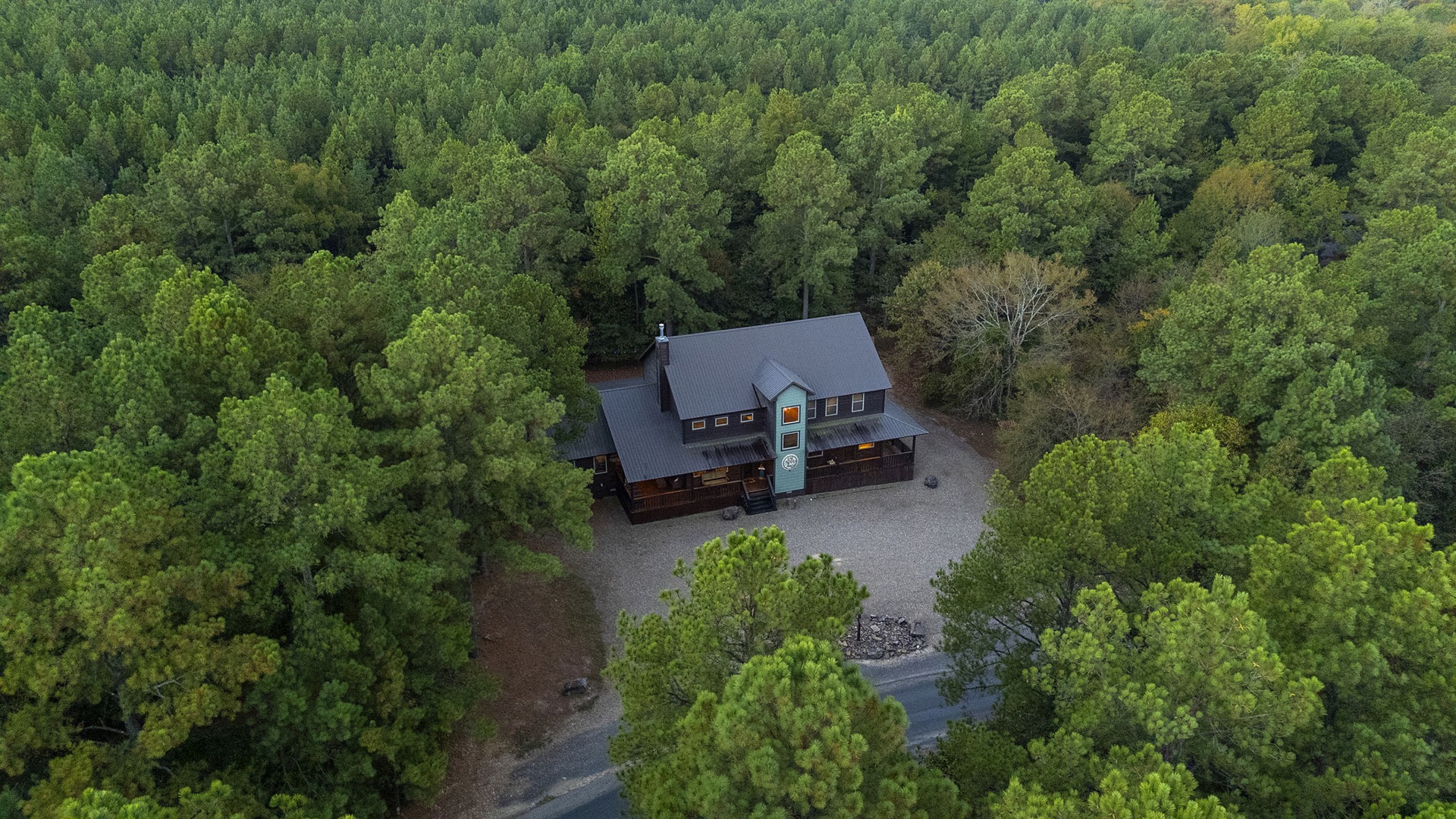 A secluded retreat nestled among lush forest, offering peaceful seclusion and natural beauty. The property features ample parking and sits along a winding private drive.