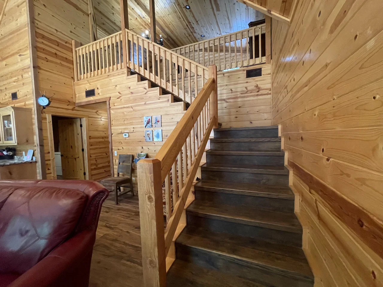 This charming cabin interior invites you to unwind with its warm wood tones and open loft layout. The handcrafted staircase leads to your cozy upstairs retreat, while natural light fills every corner.