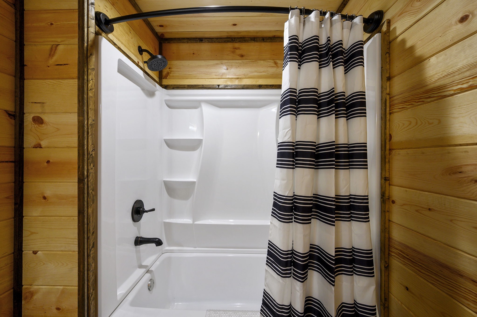 Step into your private bathroom with a pristine tub-shower combo framed by warm wood paneling that adds rustic charm to your morning routine.