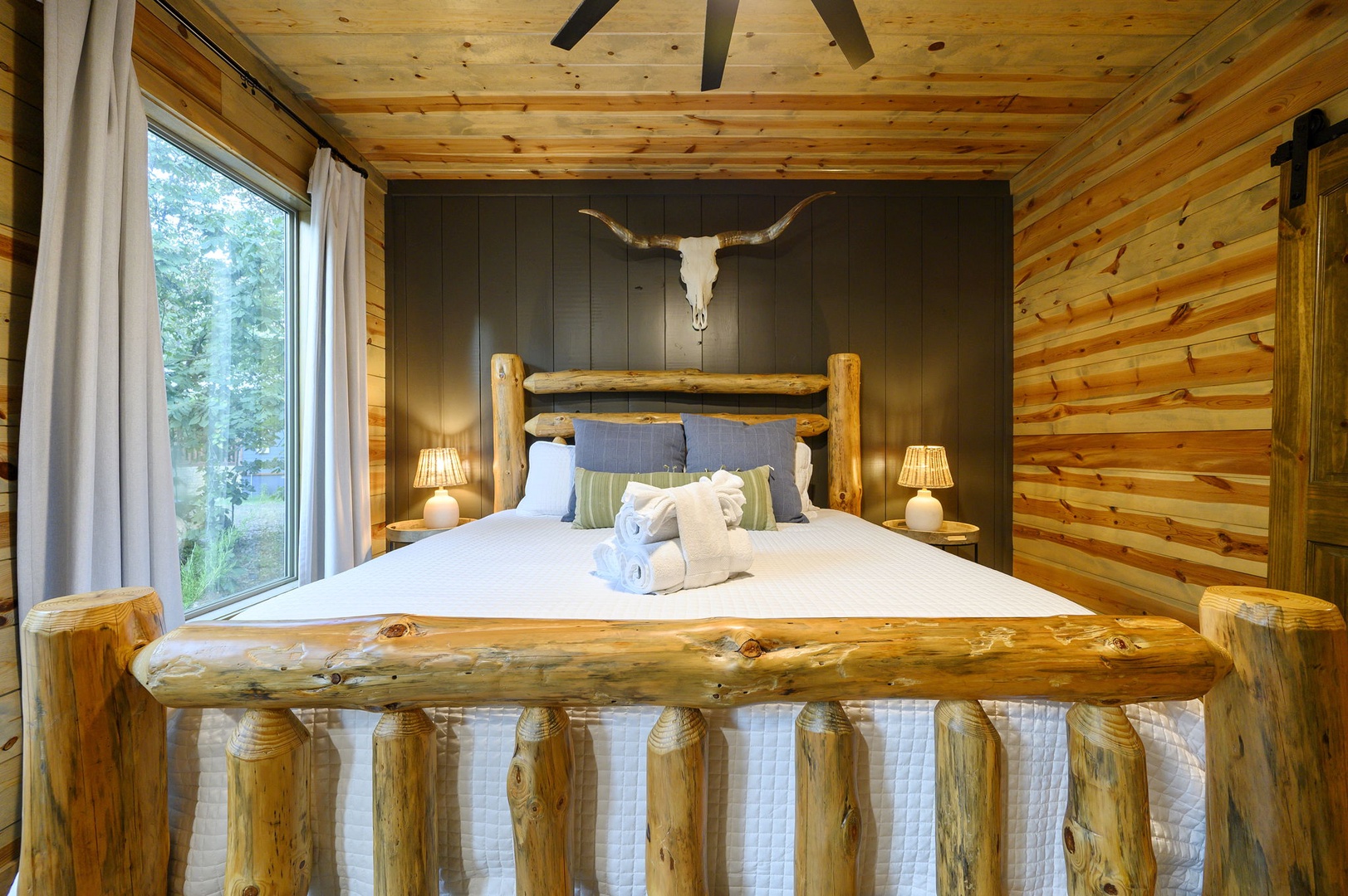 Sink into handcrafted rustic charm in your secluded bedroom, where natural wood and a custom log bed invite deep, restful sleep surrounded by peaceful woodland views.