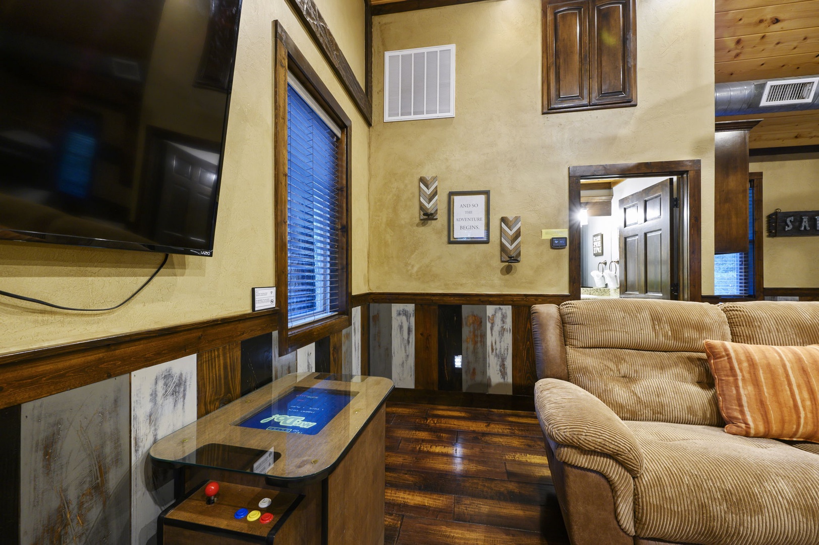 Unwind in your welcoming living space with plush corduroy seating, warm wood accents, and a vintage arcade table for entertainment—your rustic escape awaits.