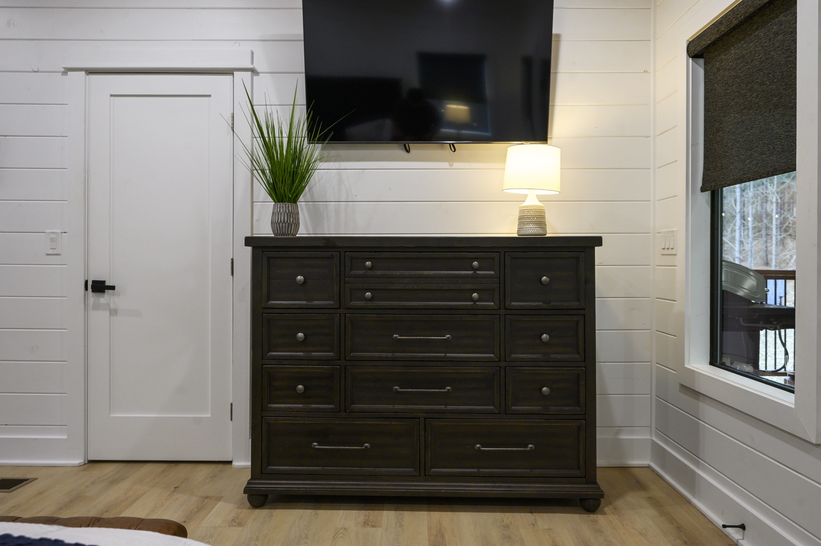 Your cozy bedroom features a thoughtfully arranged dark wood dresser beneath a wall-mounted TV, creating the perfect spot for relaxing.
