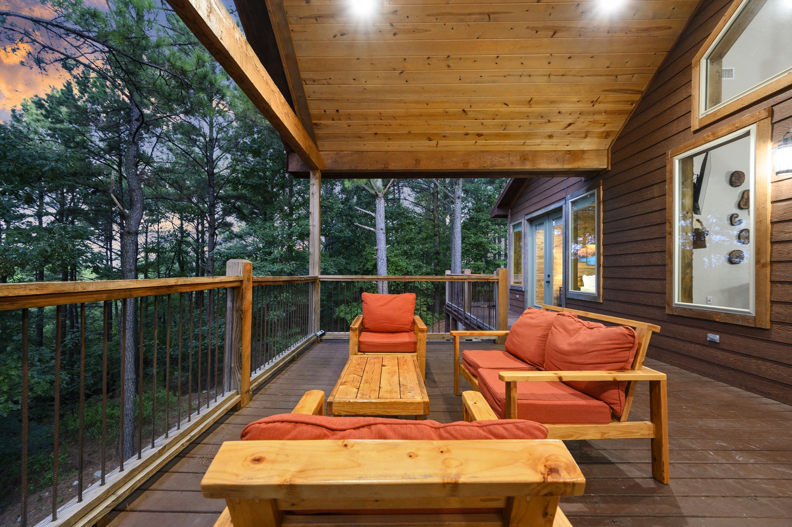 Sink into soft cushions and breathe in the fresh forest air from your private covered deck, where towering pines frame your peaceful retreat and twilight glows through the trees.
