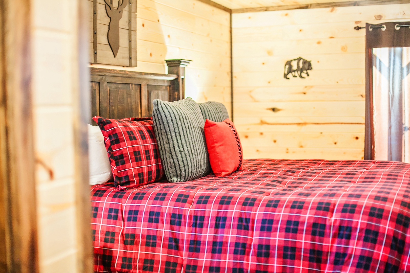 Snuggle into your cozy cabin bedroom with warm red plaid bedding, rustic wood walls, and charming woodland touches for the perfect mountain retreat.