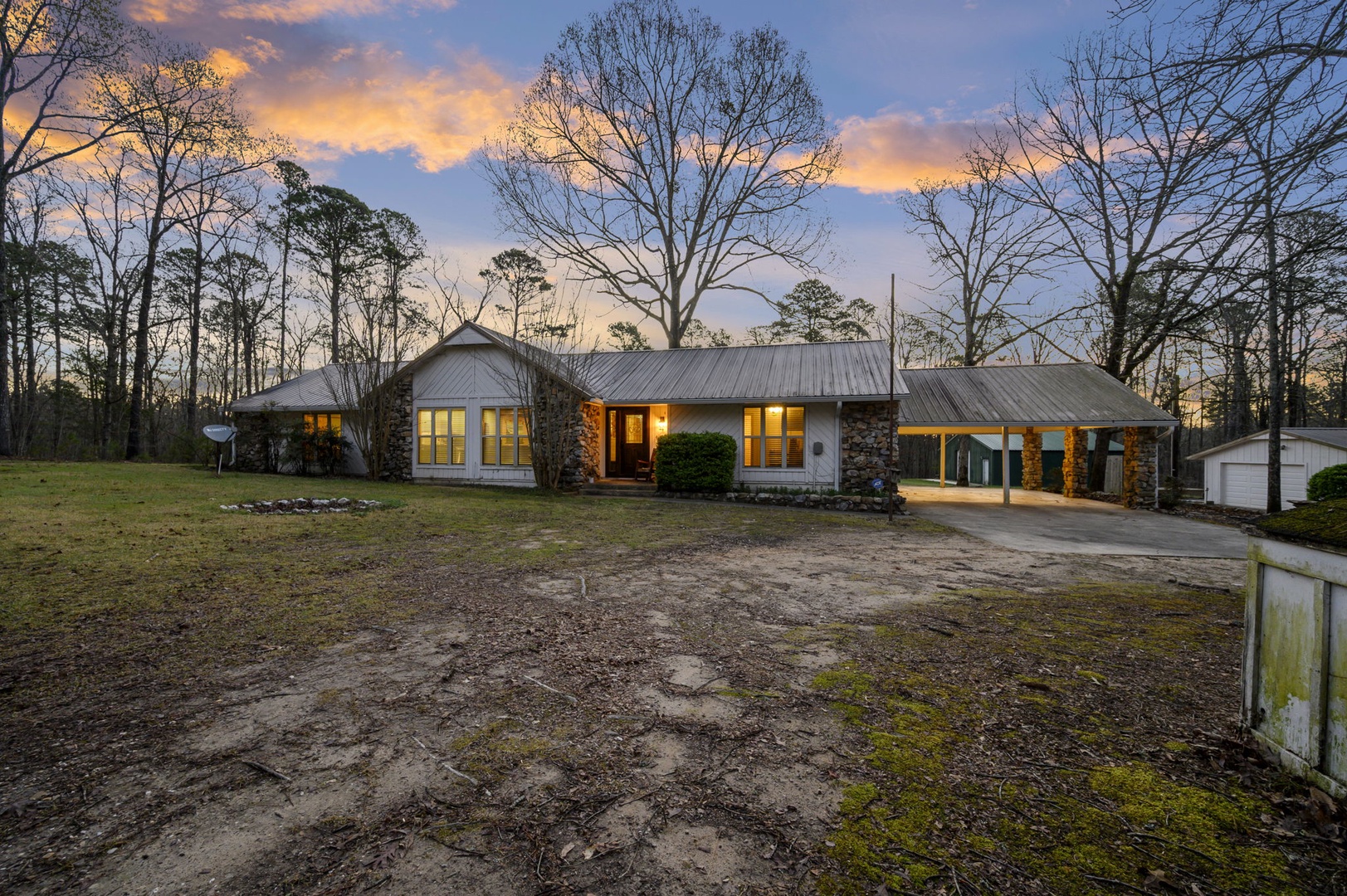 Charming ranch-style home nestled among towering trees with warm evening lighting and private wooded setting.