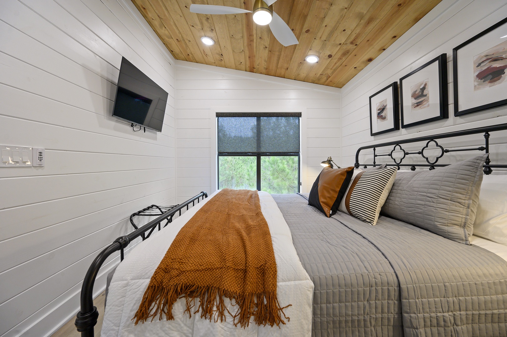 Unwind in your cozy bedroom featuring white shiplap walls, warm wood ceiling, and a plush bed with stylish linens perfect for restful nights.