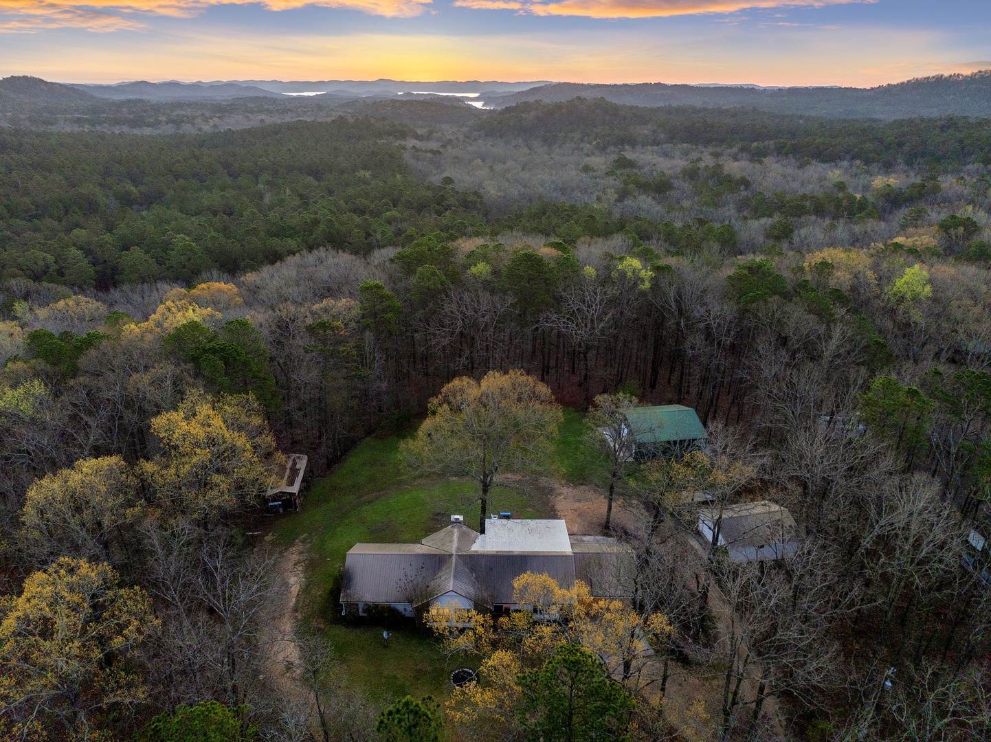 Aerial view of a secluded property nestled among rolling hills and natural landscape at sunset.