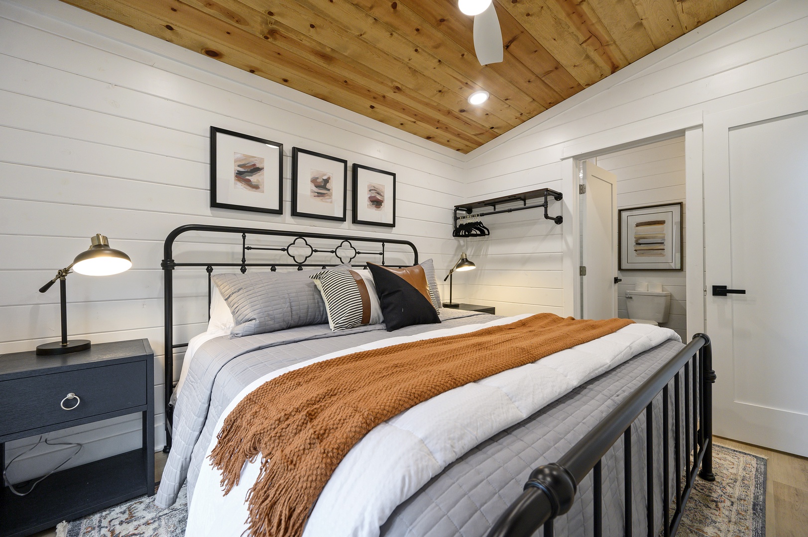 Cozy farmhouse bedroom with rustic wood ceiling, crisp linens, and warm accents—your perfect retreat awaits.