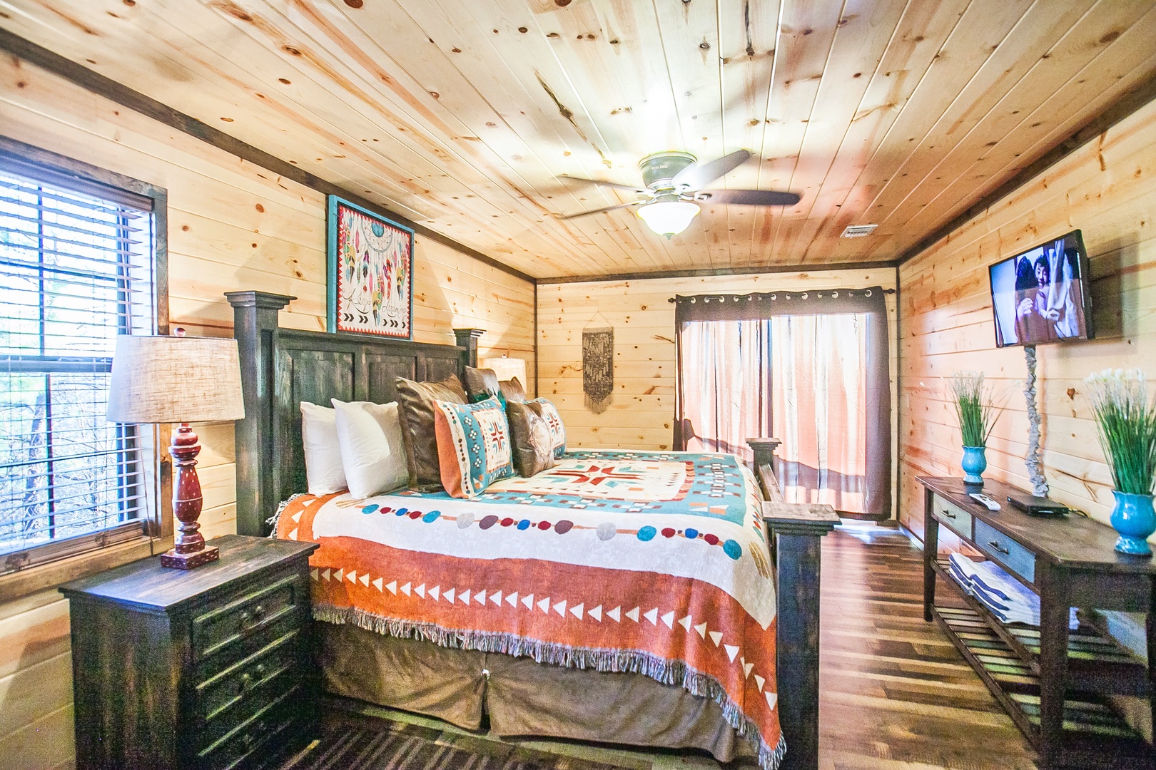 Unwind in your rustic bedroom featuring authentic log walls, colorful Native American-inspired bedding, and modern amenities like TV and air conditioning.