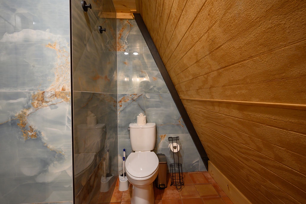 Step into this cozy powder room with warm wood tones and elegant marble-inspired tile. Your private retreat features a sleek glass-enclosed shower and thoughtful touches like a tissue holder and decorative accents.