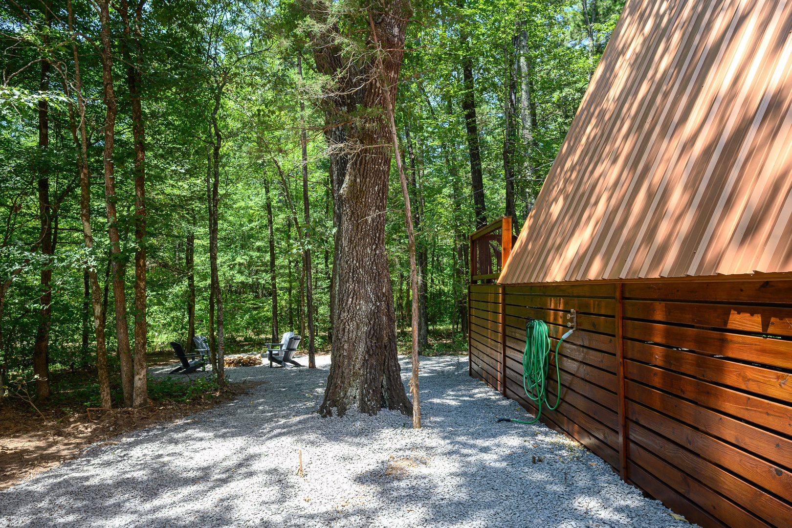 This A-frame cabin nestled among tall trees offers peaceful forest surroundings. A gravel pathway leads past comfortable outdoor seating where you can relax and soak in the natural beauty.