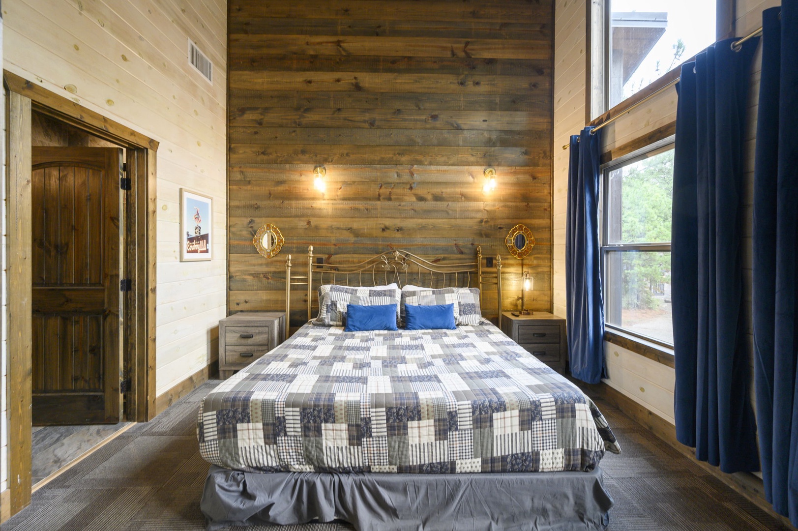 Sink into your plush bed beneath warm sconce lighting and rustic wood paneling, where high ceilings and natural light through large windows create a restful retreat.