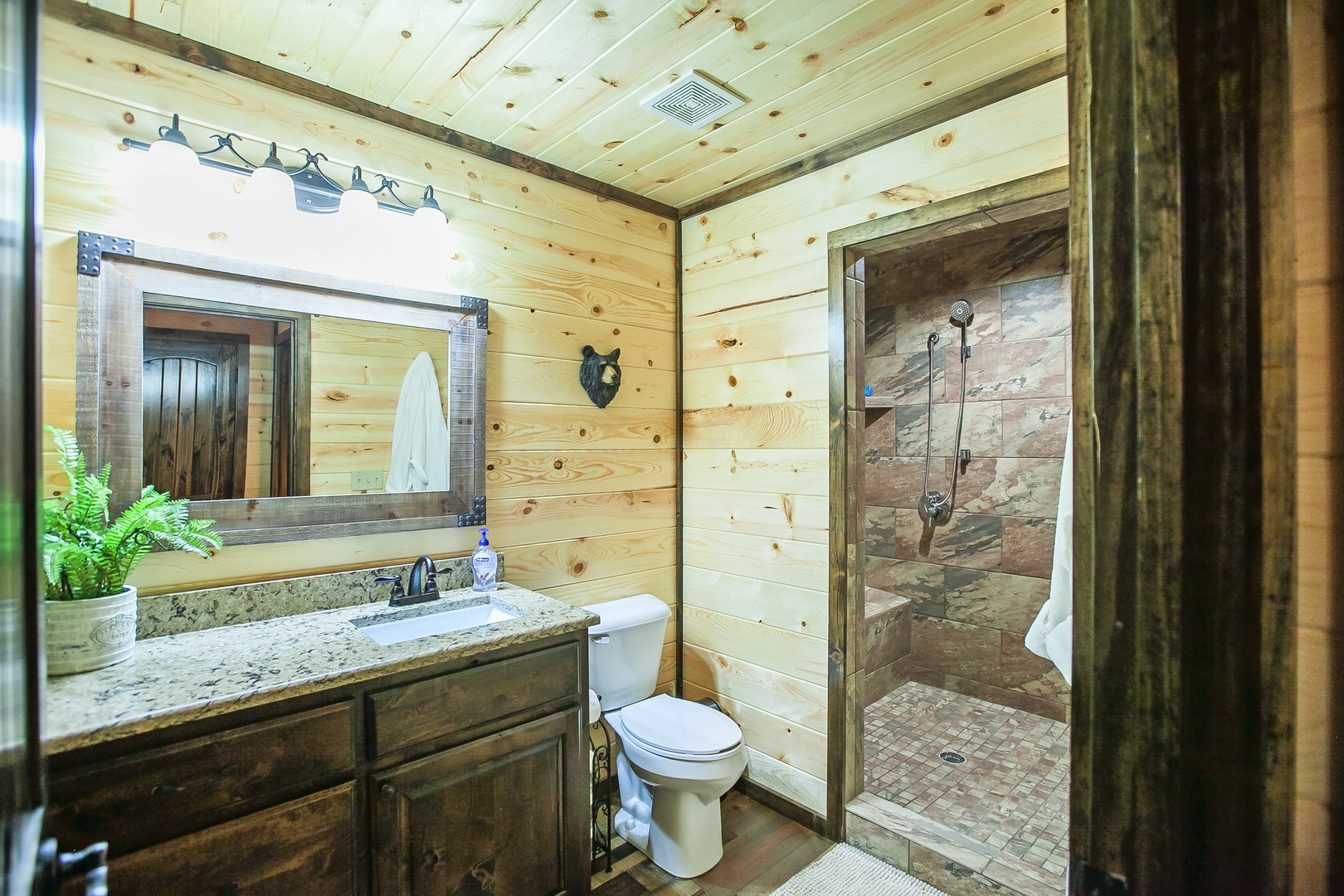 Step into your rustic cabin bathroom with natural wood walls, granite countertops, and a beautiful stone-tiled shower that makes you feel at home in nature.