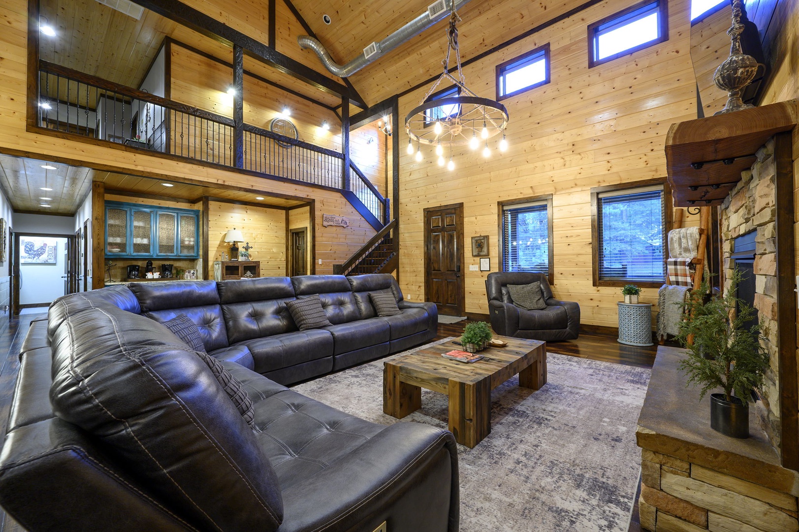 Step into this inviting open-concept living room, where soaring wood-paneled ceilings and a cozy stone fireplace create the perfect mountain retreat for your relaxation.
