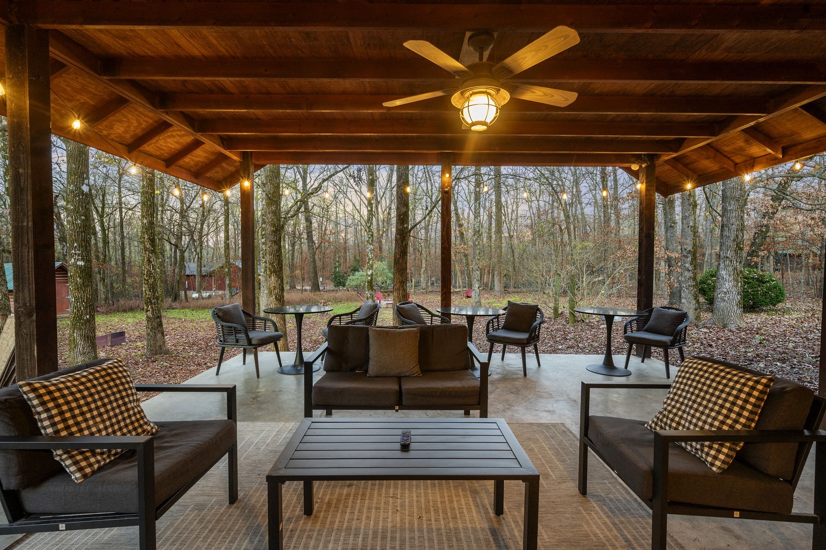 Unwind in your covered pavilion where plaid pillows and cozy seating create the perfect forest retreat for morning coffee or evening conversations.