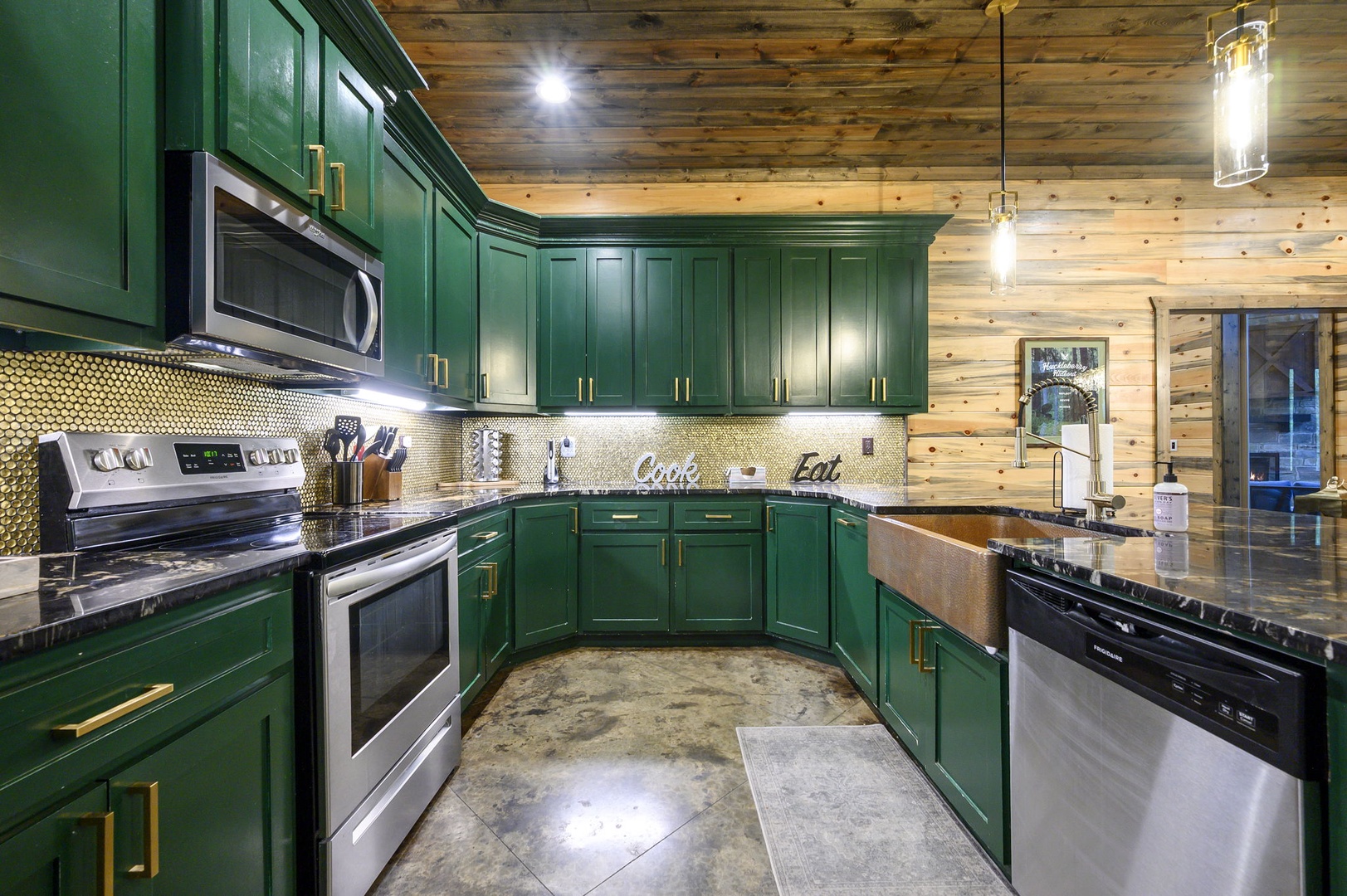 Rich green cabinetry meets warm wood plank ceilings in your fully-equipped mountain retreat kitchen, where stainless steel appliances and gleaming countertops invite you to cook and gather.