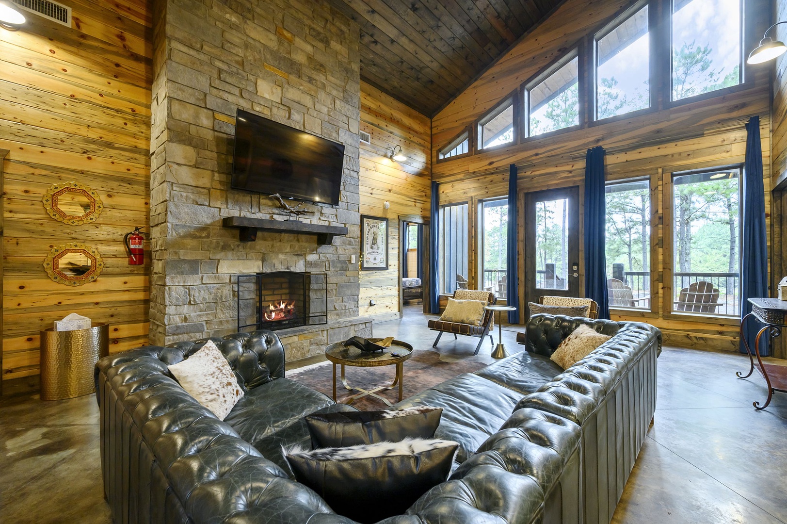 Gather around the glowing fireplace in this soaring great room, where rustic wood beams, stone walls, and plush leather sofas create your perfect mountain retreat. Floor-to-ceiling windows frame views of the surrounding pines.